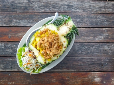 Thai style pineapple fried rice served in a pineapple on a woode