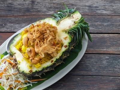 Thai style pineapple fried rice served in a pineapple on a woode