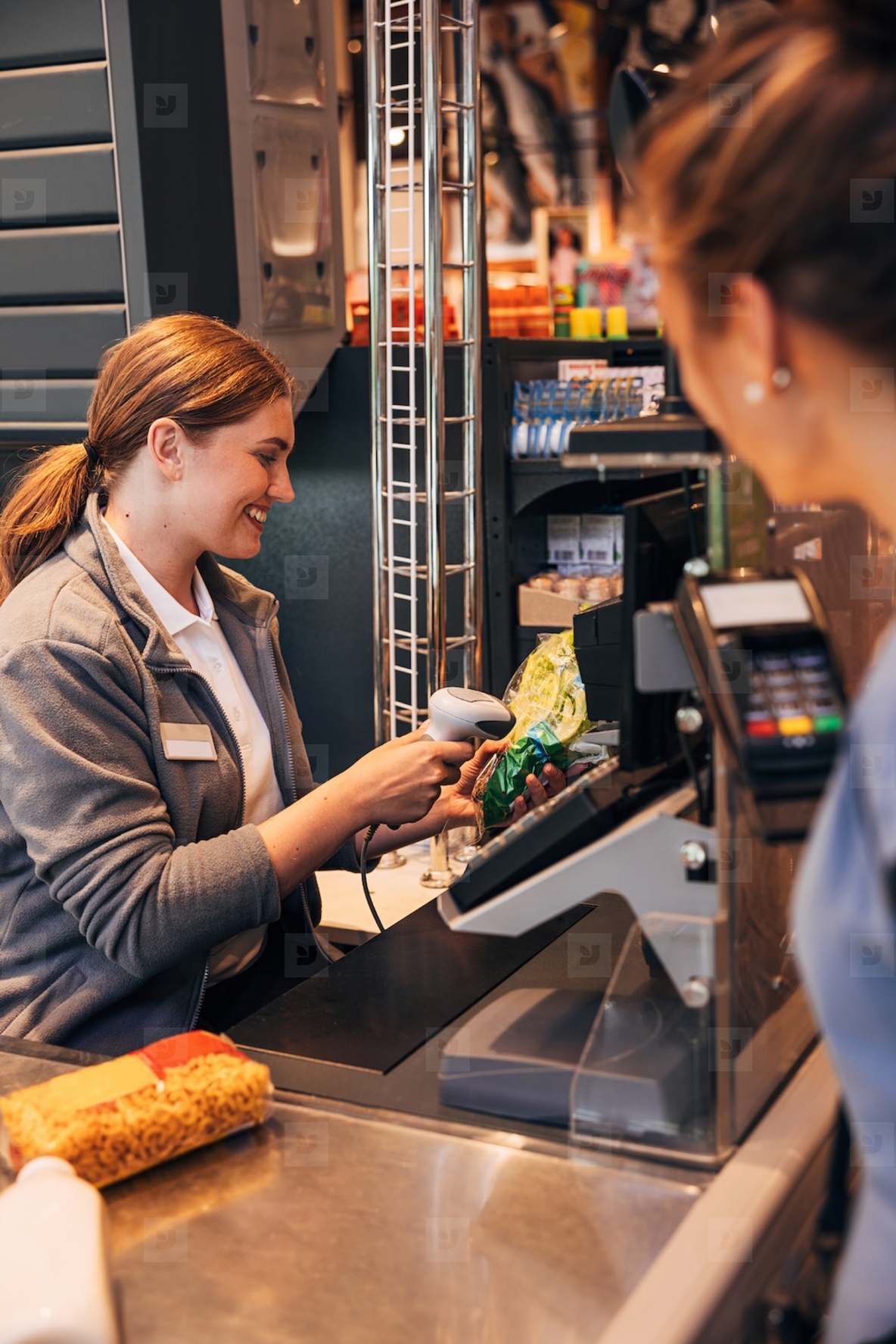 Smiling cashier using a barcode scanner on a salad pack while customer waiting