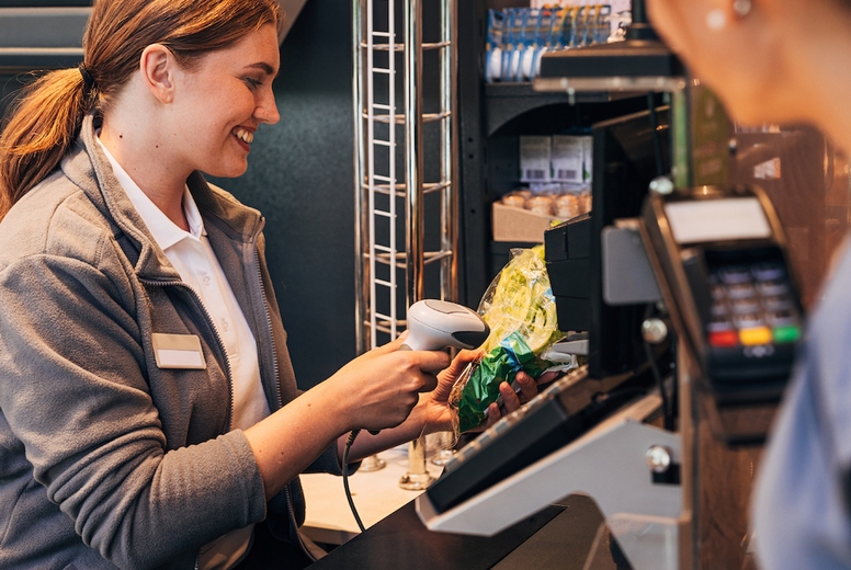 Smiling cashier using a barcode scanner on a salad pack while customer waiting