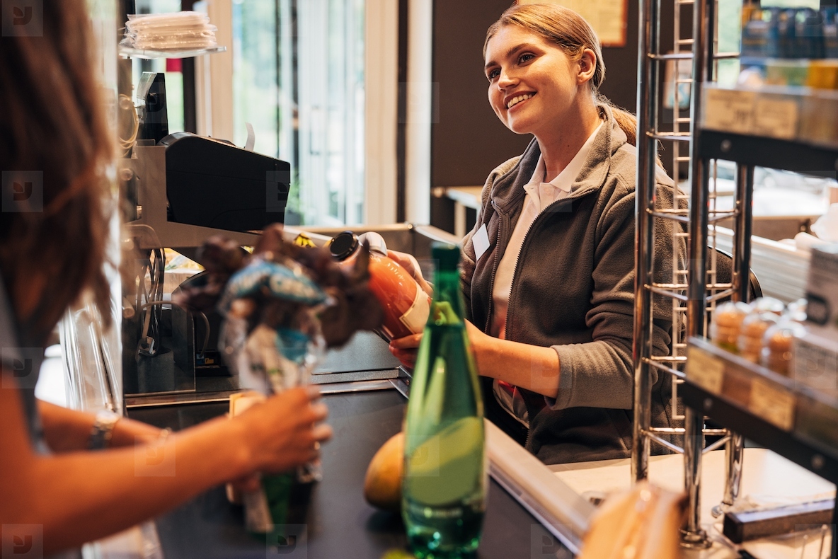 Young smiling woman working as a cashier  holding a bottle and using a barcode scanner