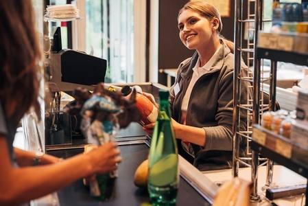 Young smiling woman working as a cashier  holding a bottle and using a barcode scanner