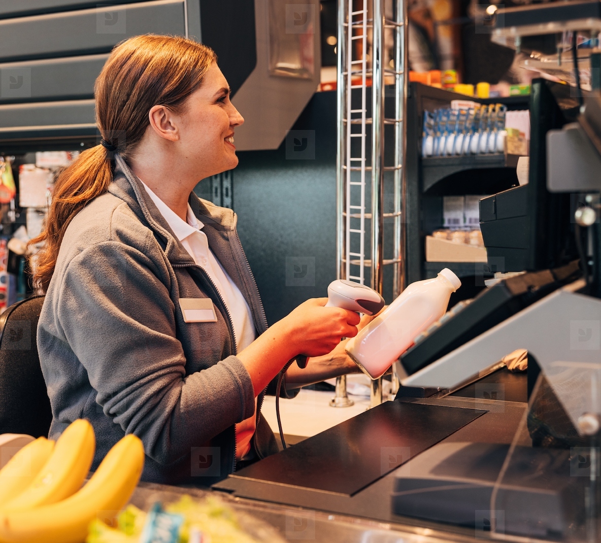 Smiling cashier using a barcode scanner on a bottle of milk in a grocery store