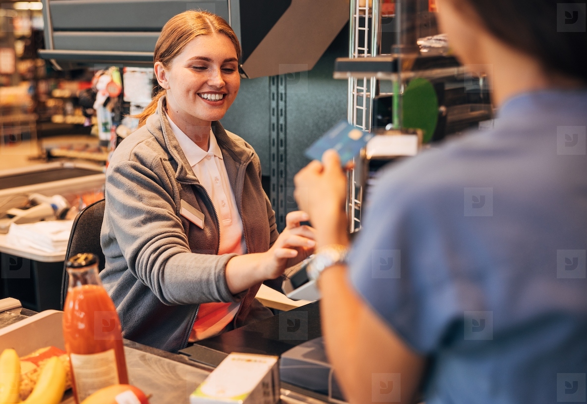 Smiling cashier in a grocery store receiving payment from a customer using pos terminal