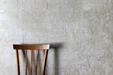 A minimalistic photo of a wooden chair with vertical slats placed against a textured concrete wall