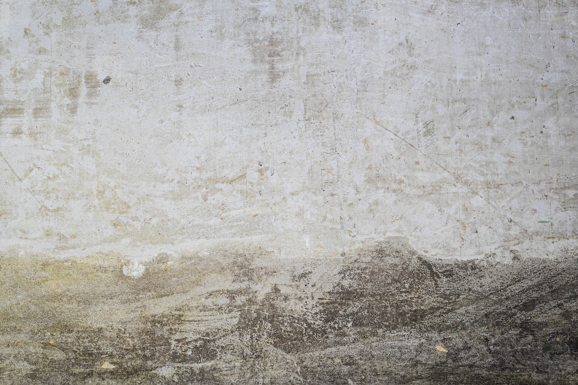 A close up photo of a textured concrete wall with visible stains  scratches  and weathered marks  The rough surface shows natural patterns and grunge details
