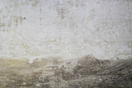 A close up photo of a textured concrete wall with visible stains  scratches  and weathered marks  The rough surface shows natural patterns and grunge details