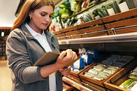 Young woman working in a grocery store holding a digital tablet