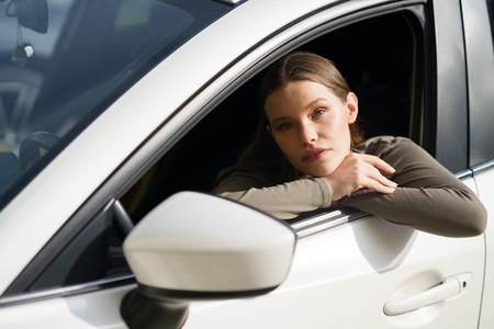 A Pensive Young Woman Sitting in a Car and Looking Out the Window Lost in Thought