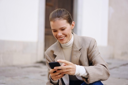 A Joyful Woman Engaged Enthusiastically with Her Smartphone While in an Urban Setting A Joyful Woman Engaged Enthusiastically with Her Smartphone While in an Urban Setting