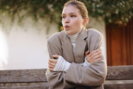 A Woman Sitting on a Park Bench  Wearing a Cozy Sweater  Feels Cold During Autumn Days