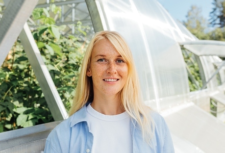 Smiling woman with blond hair and freckles standing at a greenhouse  Highly detailed portrait of a greenhouse worker standing outdoors