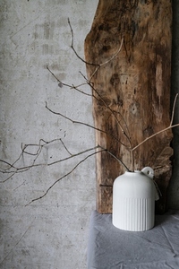 Minimalist still life with a white ceramic vase holding dry branches  placed against a rustic wooden board and textured concrete wall  Natural wabi sabi style composition