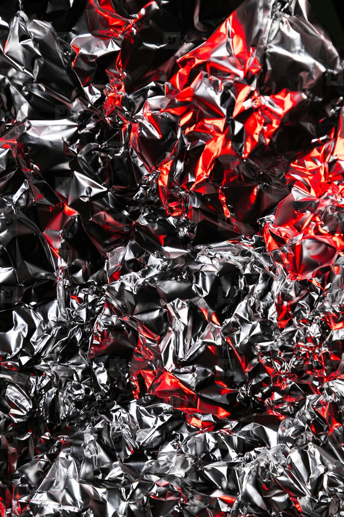 Close up of crumpled aluminum foil with shiny silver surface and dramatic red highlights  Abstract metallic background with reflective texture and artistic light play