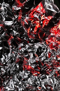 Close up of crumpled aluminum foil with shiny silver surface and dramatic red highlights  Abstract metallic background with reflective texture and artistic light play