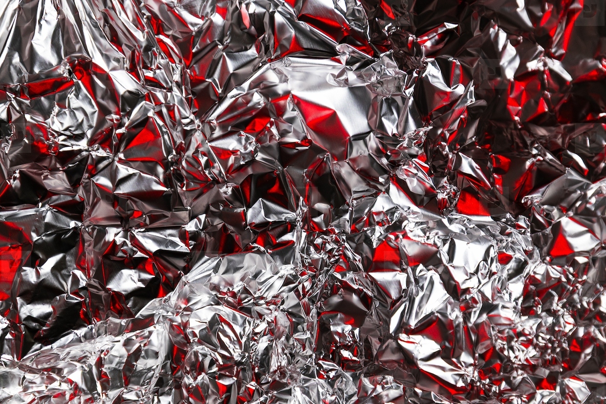 Close up of crumpled silver foil with red reflections creating an abstract textured background Shiny metallic surface with vibrant contrast and modern artistic look