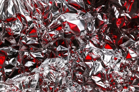 Close up of crumpled silver foil with red reflections creating an abstract textured background  Shiny metallic surface with vibrant contrast and modern artistic look