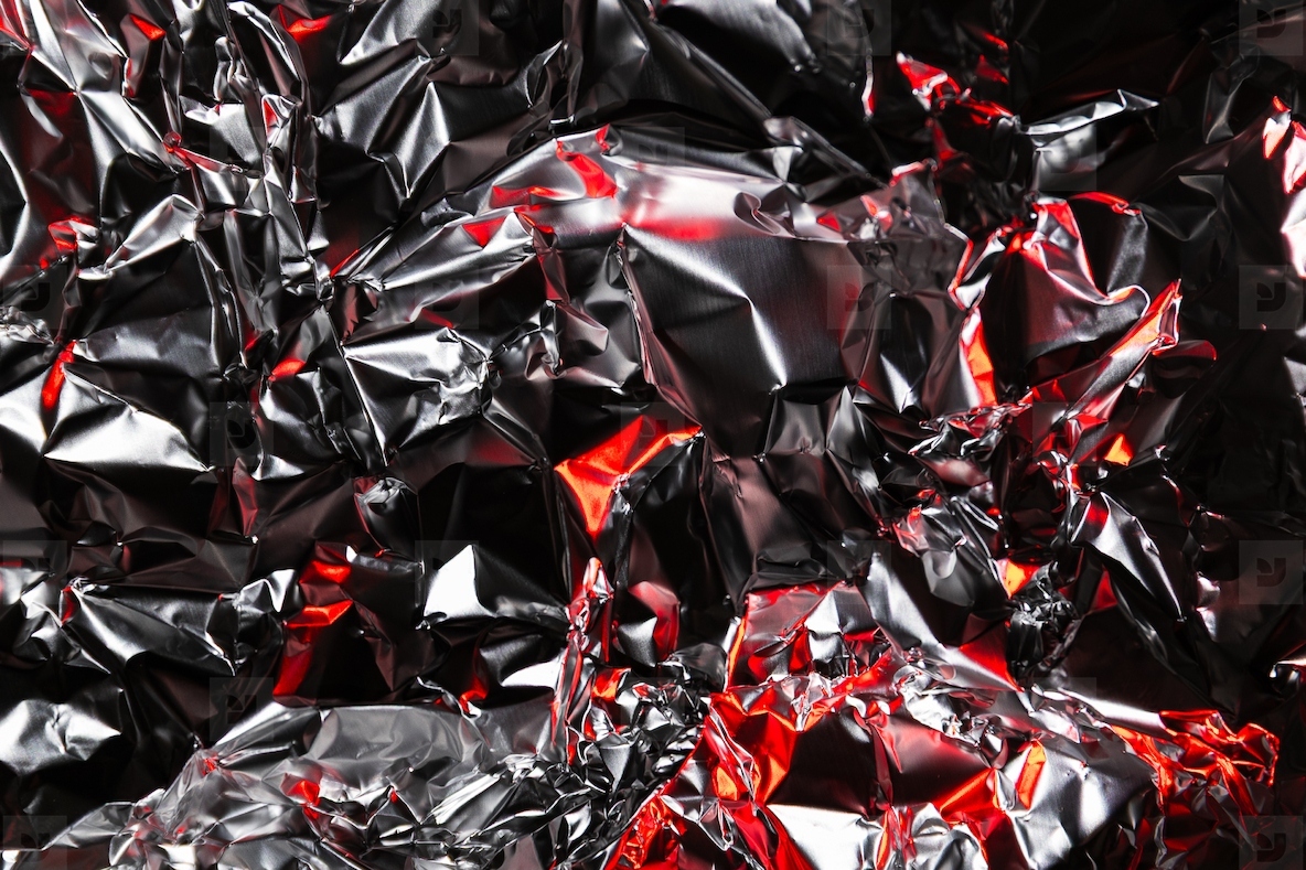 Close up of crumpled aluminum foil with shiny silver surface and dramatic red highlights  Abstract metallic background with reflective texture and artistic light play
