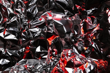 Close up of crumpled aluminum foil with shiny silver surface and dramatic red highlights  Abstract metallic background with reflective texture and artistic light play