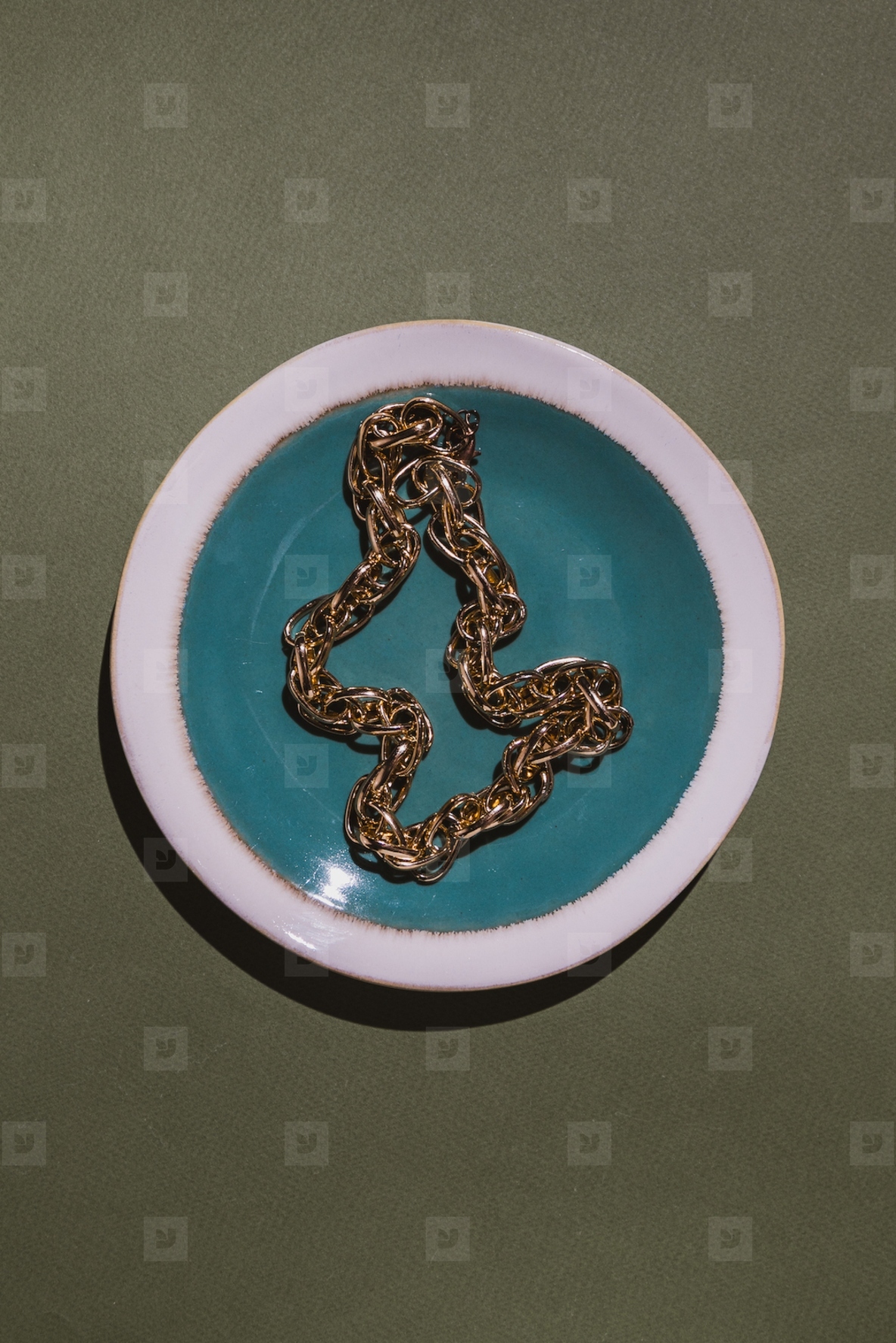 Vintage gold chain displayed in a ceramic plate with teal glaze on a green background  Minimalist still life composition with retro charm