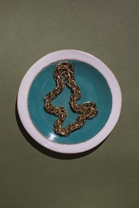 Vintage gold chain displayed in a ceramic plate with teal glaze on a green background  Minimalist still life composition with retro charm