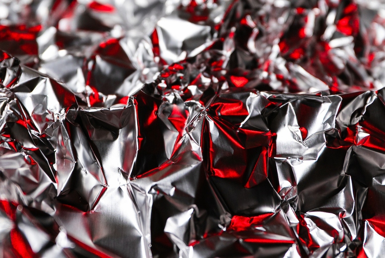 Shiny crumpled foil with silver and red reflections creating a metallic abstract design. Futuristic texture with chrome surface and cyberpunk background style