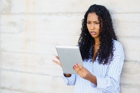 A woman is focused on her tablet  leaning against a wall  reflecting modern digital life