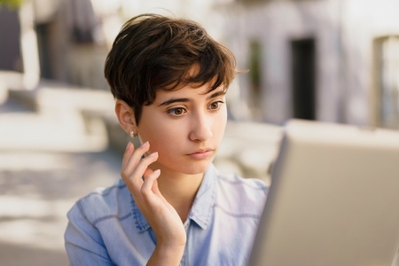 A thoughtful young person deeply engaged with their laptop while enjoying the outdoors