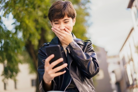 Joyful Moment A Young Person Laughing Heartily at Their Smartphone in a Vibrant Urban Setting
