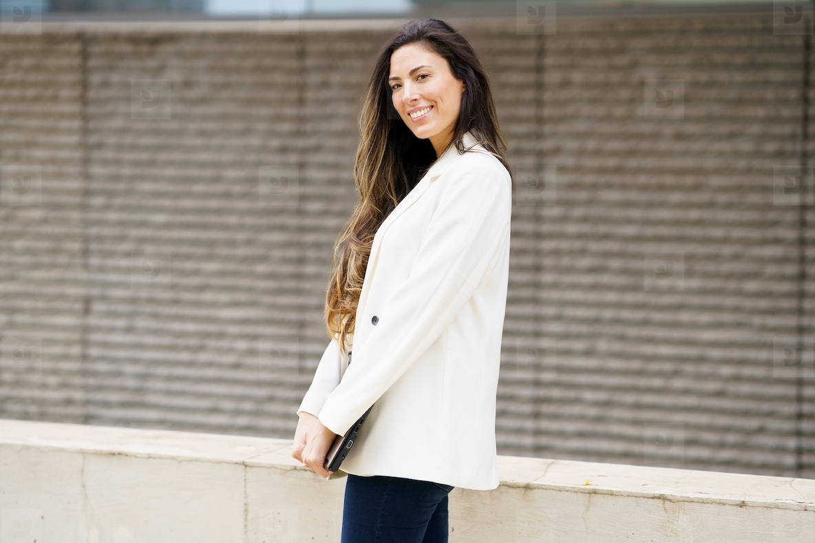 A Smiling Young Woman Dressed in a Stylish Blazer Poses Against a Modern Urban Background