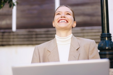 A Joyful Businesswoman Smiling Outdoors While Using Her Laptop with a Positive Outlook