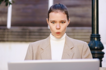 A surprised businesswoman is diligently working on her laptop outdoors in a casual setting