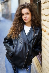A Stylish Young Woman with Curly Hair  Dressed in a Black Leather Jacket and Radiating Confidence