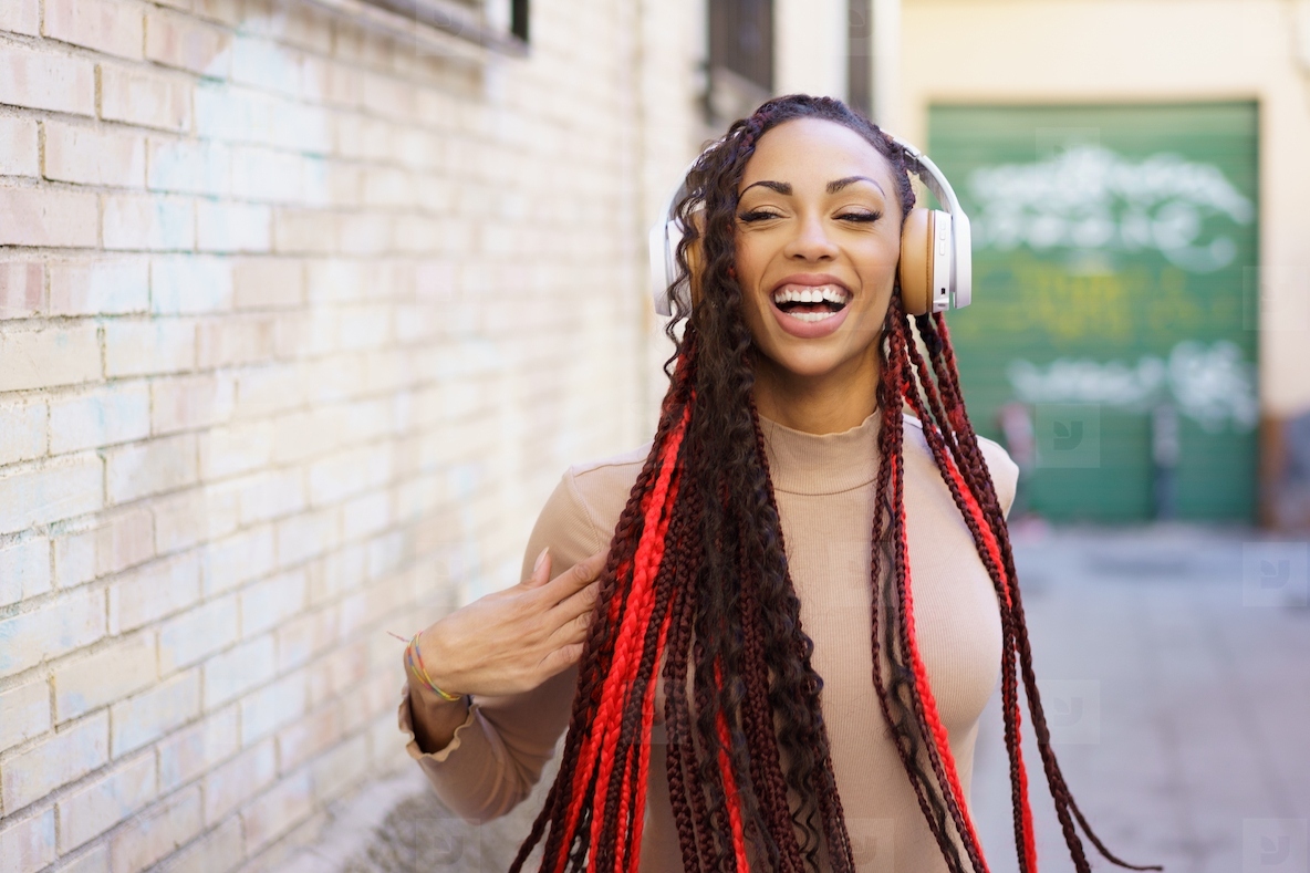 A Joyful Woman with Braids Delightfully Enjoying Music While in a Vibrant Urban Setting