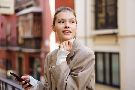 A Young Woman is Happily Enjoying a Leisurely City Stroll while Holding a Smartphone in Hand A Young Woman is Happily Enjoying a Leisurely City Stroll while Holding a Smartphone in Hand
