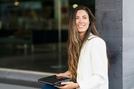 A Smiling Woman Enjoying a Coffee Break while Working on Her Laptop in an Urban Setting