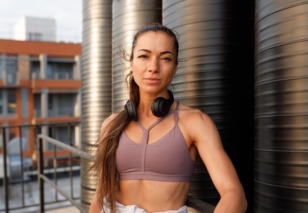 High detailed portrait of a young sportswoman wearing wireless headphones  Female in sportswear standing outdoors at sunset and looking at camera  High detailed portrait of a young sportswoman wearing