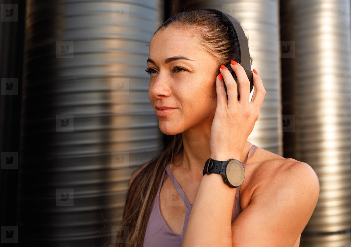 Side view of a muscular female with wireless headphones outdoors during a workout