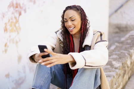 A young woman sits outdoors with her smartphone enjoying the fresh air and vibrant atmosphere A young woman sits outdoors with her smartphone enjoying the fresh air and vibrant atmosphere