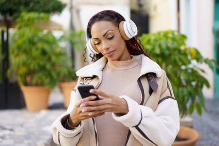 A Young Woman Joyfully Enjoying Her Favorite Music While Outdoors Using a Smartphone with Headphones A Young Woman Joyfully Enjoying Her Favorite Music While Outdoors Using a Smartphone with Headphones