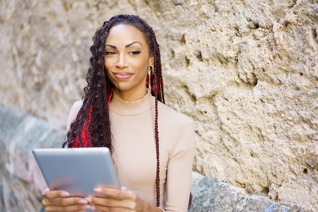 A Confident Woman Engaged in Using a Tablet While Seated Against a Stone Wall Background
