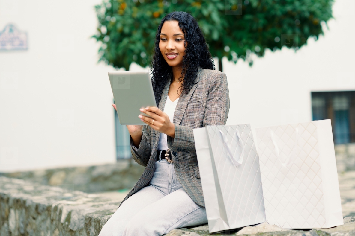 A Stylish Woman Engaging in Online Shopping Using Her Tablet While Surrounded by Shopping Bags