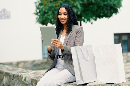 A Stylish Woman Engaging in Online Shopping Using Her Tablet While Surrounded by Shopping Bags