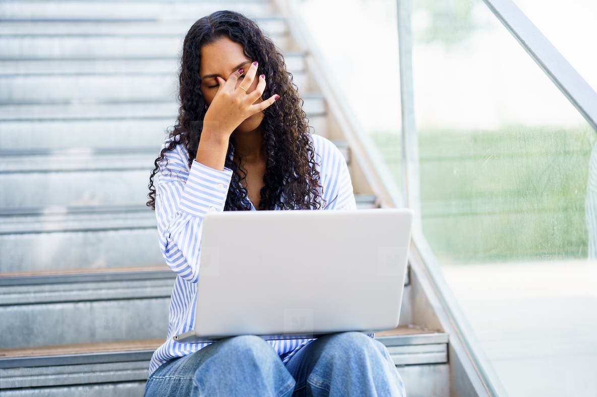 A woman experiencing stress works on her laptop in a modern  stylish indoor setting