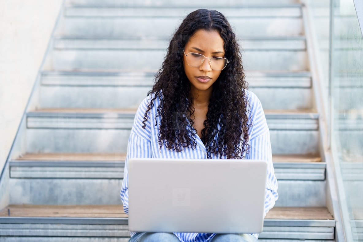 A Focused Young Woman Engaged in Working on Her Laptop While Sitting Comfortably on Stairs