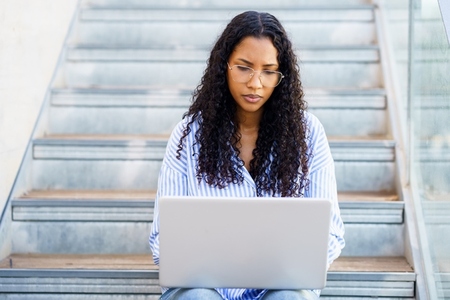 A Focused Young Woman Engaged in Working on Her Laptop While Sitting Comfortably on Stairs