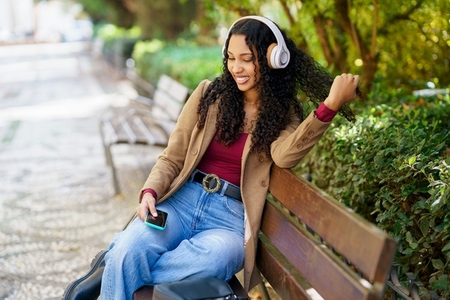 A young woman is happily enjoying some music while sitting in the park with headphones on A young woman is happily enjoying some music while sitting in the park with headphones on