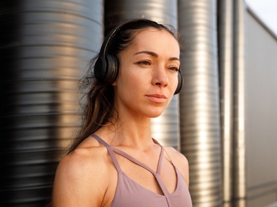 High detailed portrait of young female wearing wireless headphones standing outdoors at sunset