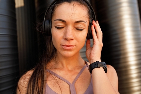 High detailed close up portrait of a young sportswoman with long hair enjoying music with closed eyes