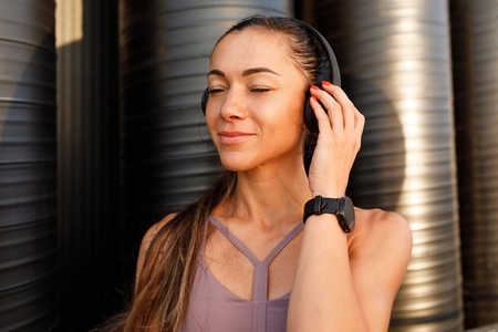 Satisfied young sportswoman with wireless headphones listening to music with closed eyes